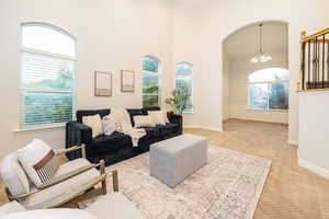 Living area with a chandelier, light carpet, a high ceiling, arched walkways, and a wainscoted wall