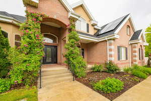 Property entrance featuring solar panels, brick siding, roof with shingles, and a porch
