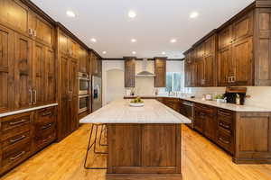 Kitchen featuring wall chimney exhaust hood, arched walkways, stainless steel appliances, a sink, and a center island