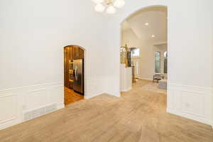 Unfurnished room featuring arched walkways, a chandelier, a decorative wall, light carpet, and wainscoting