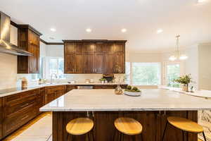 Kitchen with wall chimney range hood, a sink, ornamental molding, backsplash, and a large island