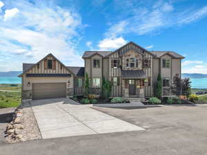 View of front of house with stone siding, board and batten siding, driveway, and a water view