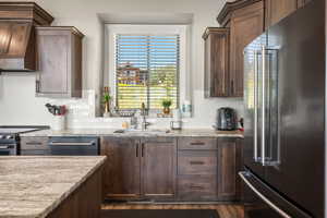 Kitchen with stainless steel appliances, custom range hood, light stone countertops, tasteful backsplash, and dark wood-type flooring