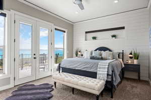 Bedroom featuring carpet flooring, access to outside, crown molding, a water view, and wooden walls
