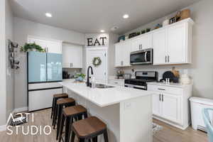 Kitchen with stainless steel appliances, a sink, light wood-type flooring, white cabinetry, and recessed lighting