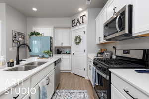 Kitchen with stainless steel appliances, a sink, light wood-style floors, light countertops, and white cabinets