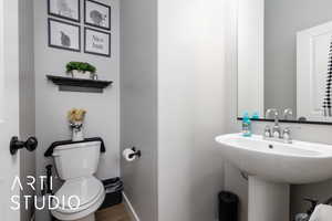 Half bathroom with toilet, a sink, wood finished floors, and baseboards
