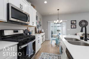 Kitchen featuring stainless steel appliances, a sink, a chandelier, white cabinetry, and light wood-style floors