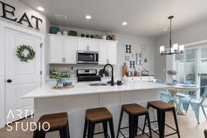 Kitchen featuring stainless steel appliances, a sink, white cabinets, a chandelier, and light wood finished floors