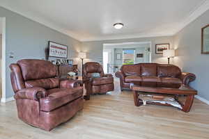 Living room with crown molding, light wood-type flooring, and baseboards