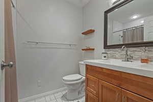 Bathroom featuring tasteful backsplash, toilet, baseboards, vanity, and curtained shower
