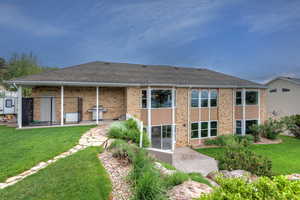 Back of house featuring a lawn, brick siding, a patio, and roof with shingles