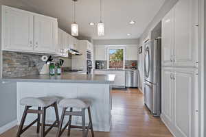 Kitchen featuring appliances with stainless steel finishes, a peninsula, under cabinet range hood, recessed lighting, and white cabinetry