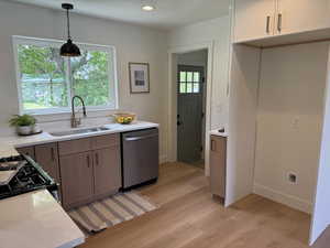 Kitchen with a sink, stainless steel dishwasher, light wood-style floors, hanging light fixtures, and black gas stove