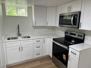 Kitchen with appliances with stainless steel finishes, a sink, white cabinets, and light wood-style floors