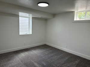 Below grade area with baseboards, dark colored carpet, and a textured ceiling
