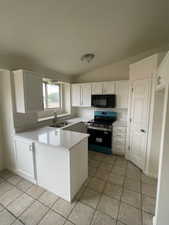 Kitchen featuring stainless steel electric stove, black microwave, a peninsula, light tile patterned floors, and white cabinetry