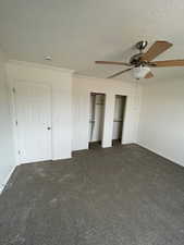 Unfurnished bedroom featuring two closets, ornamental molding, dark colored carpet, and a ceiling fan