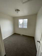Spare room featuring dark colored carpet and baseboards