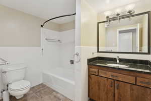Full bath with tile walls, shower / tub combination, toilet, wainscoting, and vanity