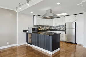 Kitchen featuring stainless steel appliances, island exhaust hood, a peninsula, backsplash, and white cabinetry