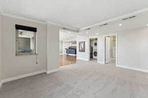 Carpeted empty room featuring stacked washing machine and dryer, crown molding, recessed lighting, and baseboards