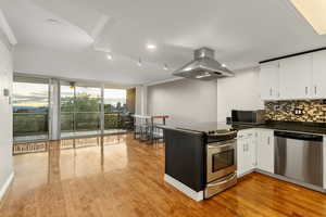 Kitchen featuring stainless steel appliances, island exhaust hood, floor to ceiling windows, dark countertops, and backsplash