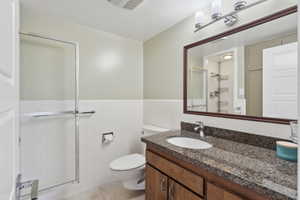 Bathroom featuring a stall shower, toilet, tile walls, vanity, and wainscoting