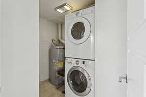 Clothes washing area featuring stacked washer / dryer, water heater, and light tile patterned flooring