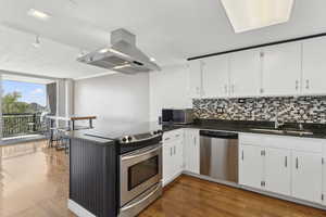 Kitchen with stainless steel appliances, a sink, island range hood, decorative backsplash, and a peninsula