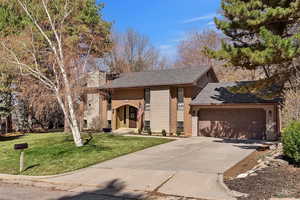 Tri-level home with driveway, a front lawn, a chimney, an attached garage, and a shingled roof