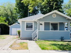 Bungalow-style house with an outbuilding, a porch, and a shingled roof
