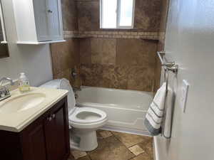 Full bathroom featuring toilet, stone finish floors, vanity, and shower / bath combination