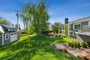 View of green lawn featuring an outdoor structure, a balcony, a patio area, and an outdoor fire pit