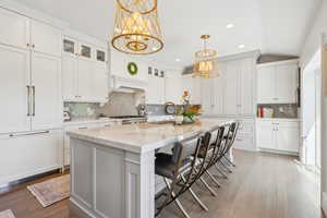 Kitchen featuring a chandelier, tasteful backsplash, white cabinetry, glass insert cabinets, and light stone countertops