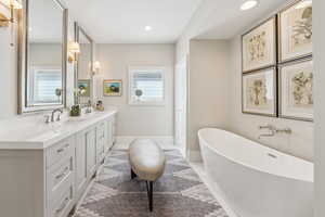 Bathroom with a freestanding bath, double vanity, recessed lighting, and baseboards