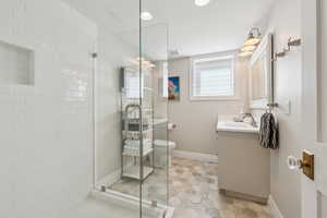 Full bathroom with tiled shower, vanity, toilet, tile patterned flooring, and baseboards