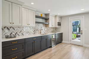 Kitchen featuring open shelves, a sink, beverage cooler, decorative backsplash, and light countertops