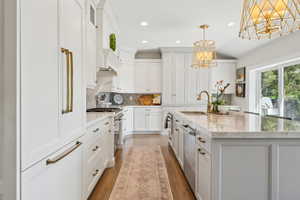 Kitchen with a sink, a chandelier, premium appliances, recessed lighting, and white cabinets