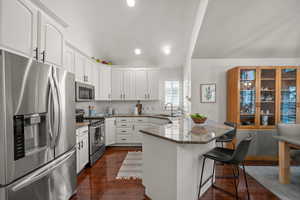 Kitchen with stainless steel appliances, a peninsula, a kitchen bar, dark stone counters, and white cabinetry
