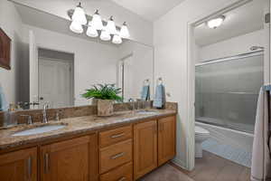 Full bathroom with toilet, bath / shower combo with glass door, double vanity, and wood finished floors