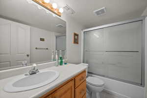 Bathroom with vanity, toilet, enclosed tub / shower combo, tile patterned floors, and a textured ceiling
