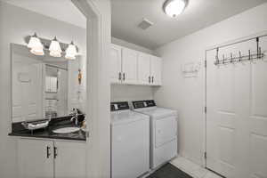 Clothes washing area with a sink, washing machine and dryer, and baseboards