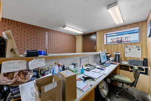 Office featuring a textured ceiling, brick wall, and wooden walls