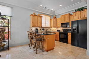 Kitchen featuring black appliances, a sink, backsplash, a breakfast bar area, and a tray ceiling