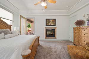 Carpeted bedroom with a tiled fireplace, ceiling fan, and baseboards