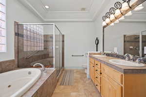 Bathroom featuring a stall shower, a jetted tub, double vanity, toilet, and a raised ceiling