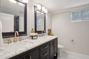 Full bath featuring toilet, double vanity, and baseboards