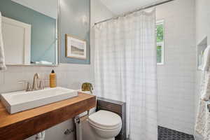 Full bathroom featuring a sink, tile walls, a tile shower, and toilet