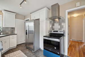 Kitchen featuring appliances with stainless steel finishes, wall chimney range hood, decorative backsplash, and white cabinetry